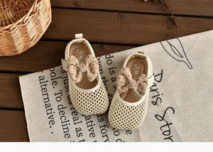 Gros plan de chaussures en maille crème pour bébé fille avec nœud à pois sur lin.