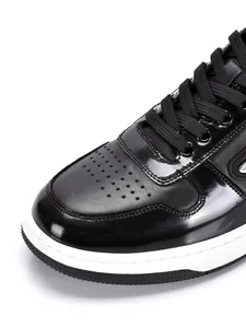 Close-up detail of black patent leather men's sneakers with perforated toe and laces