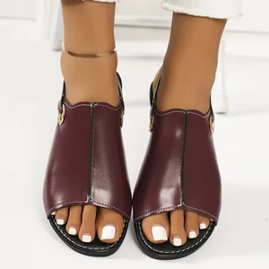 Close-up detail of burgundy flat open-toe sandals with white stitching and metal buckle.