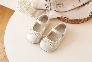 Detailed top view of white girls' bow Mary Jane princess shoes on a styled table