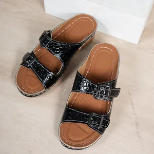 Detail of black crocodile-patterned platform slides with double buckles and white stitching.