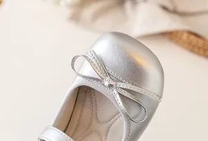 Detailed macro view of a silver girl's ballet flat with a delicate bow ornament.