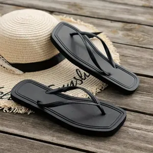 Chic black square-toe flip-flops for women on a rustic wooden deck with a straw sun hat.