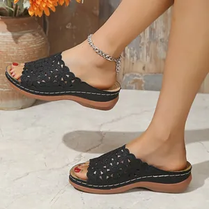 Primer plano de sandalias de cuña negras con diseño floral calado y pespuntes.