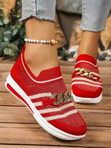 Detail view of red and white striped knit sneakers featuring a chunky gold chain ornament.