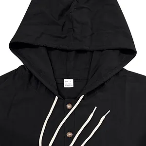 Primer plano de camisa negra con capucha de lino con cordón blanco y botones de madera