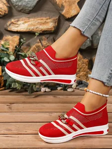 Red knit sneakers with white stripes and gold chain detail on outdoor wooden deck