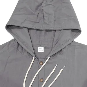 Vista detallada del escote, la capucha, el cordón y los botones de madera de una camisa de lino gris.