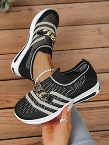 Close-up view of black and white striped fly-knit slip-on shoe with gold chain detail