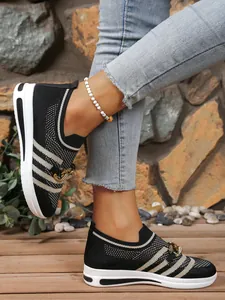 Detailed side view of stylish women's black knit sneakers with gold chain accents worn outdoors