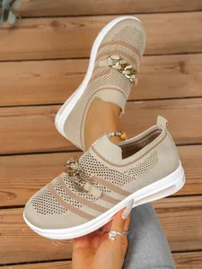 Detailed close-up view of beige knit sneakers with gold chain accent on wooden deck