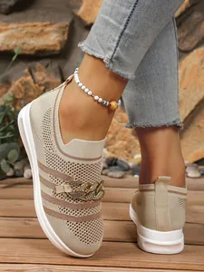 Macro view of beige fly-knit hollowed-out loafers featuring decorative gold metal chain link
