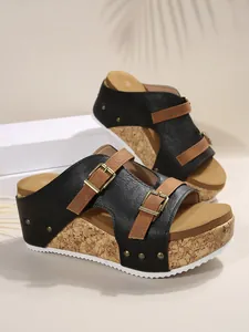 Detailed side view of stylish black wedge sandals with buckled straps and cork-patterned platform sole.
