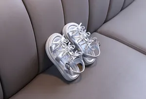 Close-up of girls' silver leather sandals with elegant rhinestone bow knots on a grey sofa