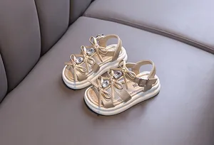 Close-up of elegant girls' gold sandals with rhinestone bows and thick soles.