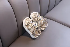 Detail of girls' champagne gold sandals with elegant bow and rhinestone accents.