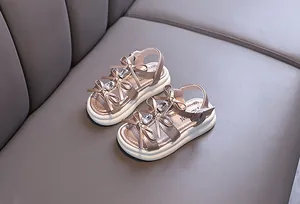 Macro detail of girls rose gold sandals featuring rhinestone bows and platform soles