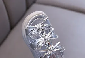 Macro detail of silver girls' sandal featuring bow ties and sparkling rhinestones