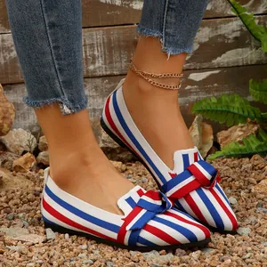 Dettaglio delle ballerine a punta in tessuto a righe rosso, bianco e blu con fiocco decorativo.