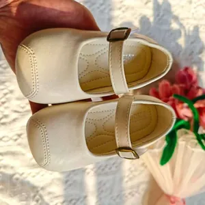 Detailansicht von cremefarbenen Baby-Mary-Janes mit Schnallenriemen und weicher Sohle.