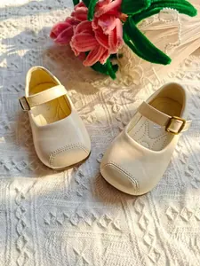 Detailansicht von beige Kinder Mary Jane Schuhen mit goldener Schnalle auf Textildecke