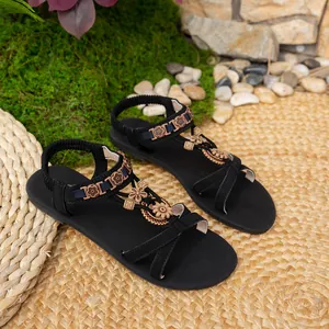 Detailansicht der schwarzen flachen Sandalen mit Holzblumen und elastischen Riemen.