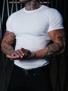 Detailed view of a white slim-fit muscle T-shirt worn by a tattooed male fitness model