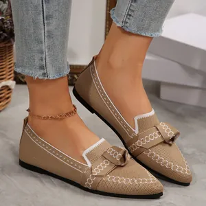 Primo piano di scarpe ballerine beige in maglia a punta con fiocco e profili bianchi.