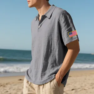 Detail van heren linnen poloshirt in grijs met Amerikaanse vlag borduursel op de mouw op strand.