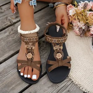 Detailaufnahme von braunen Ethno-Sandalen mit Blumenmuster und flacher Sohle auf Holzboden.