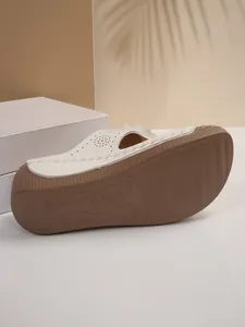 Close-up of white wedge heel sandal with floral cutouts and textured non-slip brown sole