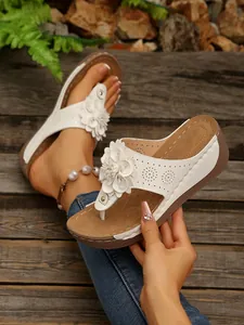 Detail view of white floral wedge slippers with ornate 3D flower and laser-cut holes
