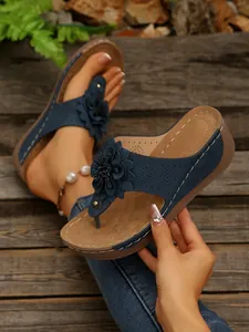 Detail view of navy blue wedge sandal featuring large floral ornament and hand detail