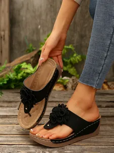 Close-up of black wedge thong sandals featuring a decorative flower on a wooden deck