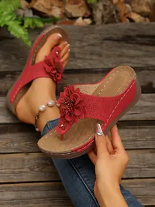 Detailed view of red wedge sandals featuring a large 3D flower and perforated strap