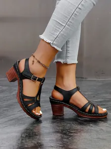 Detailansicht schwarzer T-Riemen-Römersandalen mit Blockabsatz in Holzoptik und Schnallen.
