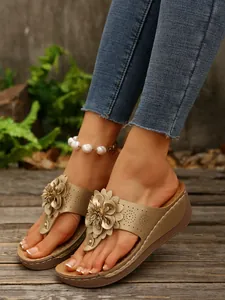 Close-up view of gold wedge flip-flops with flower decoration on model's feet.
