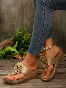 Close-up detail of champagne gold wedge flip-flop sandals with 3D floral decoration