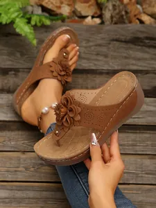 Detailed view of brown wedge flip-flops with flower decoration and contrast stitching.