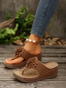 Detailed view of brown wedge thong sandals with 3D floral decoration on wooden floor