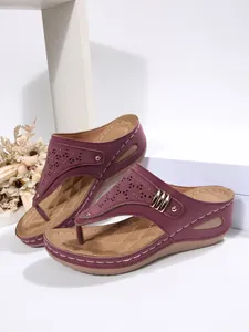 Detailed view of burgundy wedge thong sandals featuring laser-cut patterns and metal buckle