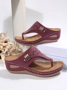 Detailed view of women's burgundy wedge thong sandals with laser-cut patterns and studs