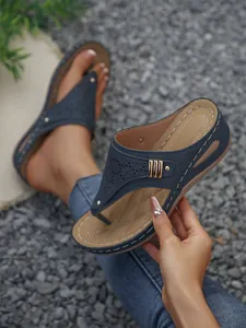 Detail of navy blue wedge thong sandals with laser-cut pattern and metal accents