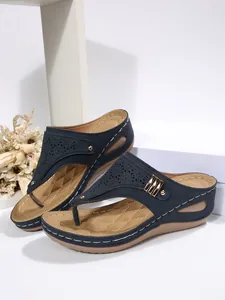 Close-up detail of navy wedge thong sandals featuring laser-cut pattern and gold rivets.