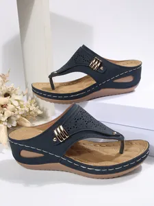 Detail view of navy blue wedge sandals with laser-cut patterns and gold rivet hardware
