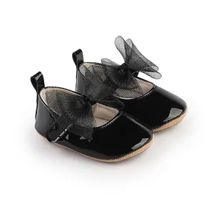 Detalle de zapatos de charol negro para bebé con un gran lazo decorativo de malla fina