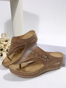 Detailed view of brown wedge flip-flop sandals with laser-cut patterns and metal studs