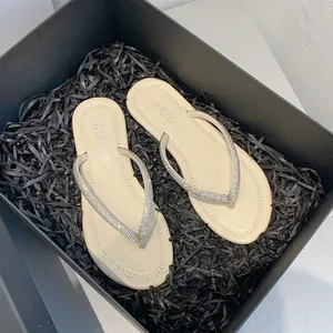 Detailed view of beige rhinestone flip-flop sandals in a premium black gift box