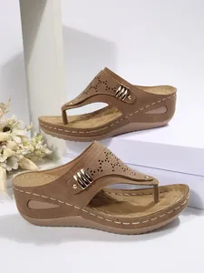 Detail view of tan women's wedge sandals with laser-cut patterns and metal rivets