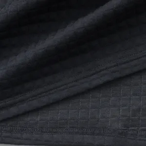 Makroansicht der schweren Jacquard-Waffelstofftextur auf einem schwarzen Herren-Poloshirt